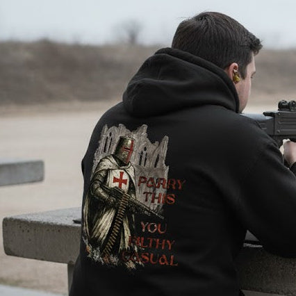 Person holding a machine gun at a shooting range with a hoodie featuring a cross and text.