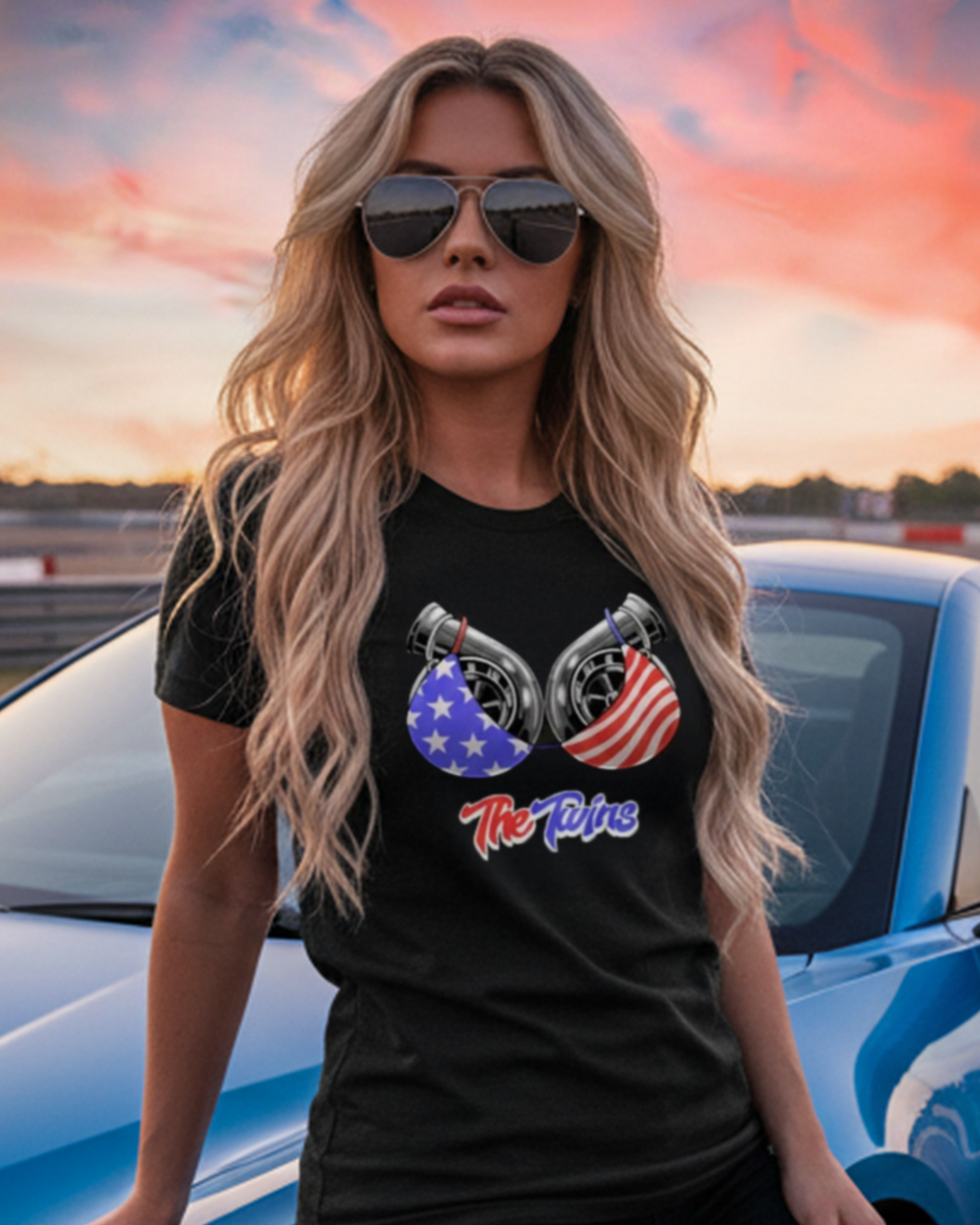 Woman posing with a blue car and automotive-themed t-shirt and hoodie on a race track background.
