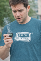 Man holding a smoking device with 'Shalom' on the screen, wearing a blue t-shirt with a similar design.
