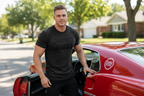 Man in a black t-shirt standing next to a red car with a visible brand logo.
