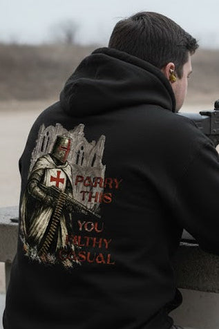 Person holding a machine gun at a shooting range with a hoodie featuring a cross and text.
